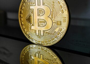 A bitcoin sits on a table in front of a mirror, reflecting the solemn nature of this cryptocurrency in relation to SEC regulations.