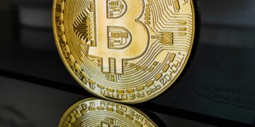 A bitcoin sits on a table in front of a mirror, reflecting the solemn nature of this cryptocurrency in relation to SEC regulations.