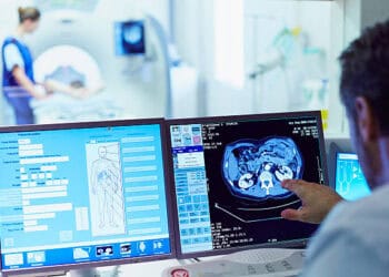 A man is looking at two monitors in a medical room while involved in a defense contract dispute.