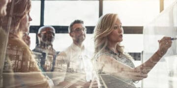 The Chief Supply Chain and Operations Officer of Perdue Foods leading a group of business people in an engaging discussion, while looking at a whiteboard.