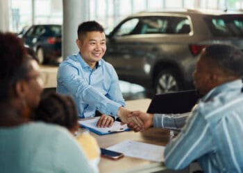 A man shaking hands with a man in a car dealership, discussing EV models.
