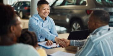 A man shaking hands with a man in a car dealership, discussing EV models.