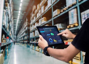 A man utilizing technology, specifically a tablet, for analytics and inventory optimization in a warehouse.