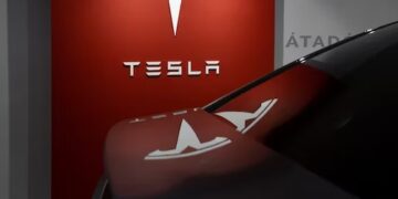 Tesla logo on a red wall with a Tesla car's rear end reflecting the logo. - Supply Chain News