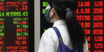 A woman wearing a face mask in front of a stock board in Tokyo.