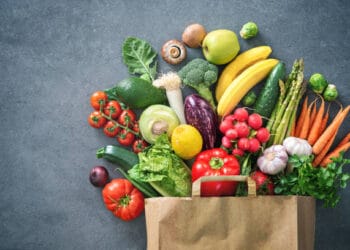 A paper bag full of vegetables and fruits on a grey background, showcasing Argentine Agricultural and Industrial Products.