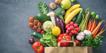 A paper bag full of vegetables and fruits on a grey background, showcasing Argentine Agricultural and Industrial Products.