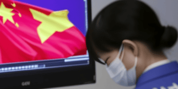 A woman wearing a face mask is looking at a computer screen with a Chinese flag while conducting an investigation for Capvision China.