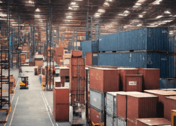Warehouse interior with stacked shipping containers; supply chain logistics and finance. - Supply Chain News
