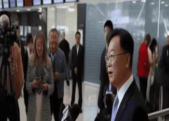 The new US Ambassador to China in a suit speaks to reporters at an airport.
