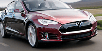 The Tesla Model S, developed by Elon Musk, is driving down the road.