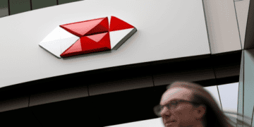 A woman walks past the HSBC building with a red and white logo.