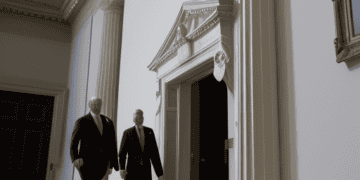 Two men in suits engaged in talks while walking down a hallway.