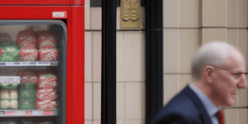 A man in a suit walking past a vending machine near a busy street.