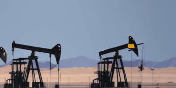Oil pumps in the desert with mountains in the background, highlighting U.S. Production Disruptions.