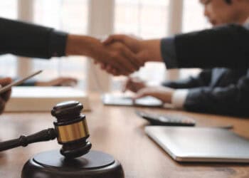 Two business people shaking hands with a judge's gavel, positively impacting veterans in the manufacturing workforce.