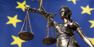 A statue of a woman holding scales in front of an EU flag symbolizes the principles of justice and balance. This visual representation can be associated with economic concepts such as interest rates and inflation forecasts, which