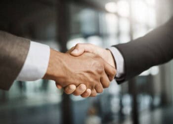 Two business people shaking hands in front of an office to celebrate the final approval of the EU-New Zealand Free Trade Agreement.