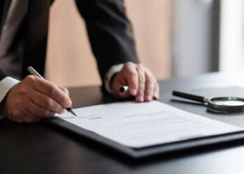A businessman from Switzerland signing a document with a magnifying glass.