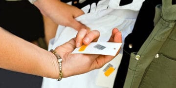 A person is holding a clothing tag on a rack, contemplating the price increase of luxury brands amidst economic challenges.