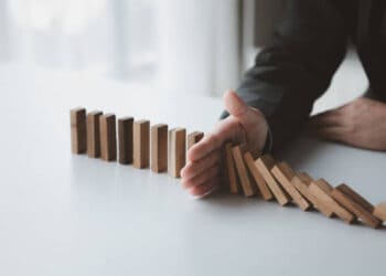 A businessman is holding dominoes on a table, contemplating the consequences of the Administration's Inflation Strategy.