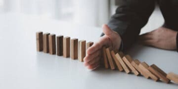 A businessman is holding dominoes on a table, contemplating the consequences of the Administration's Inflation Strategy.