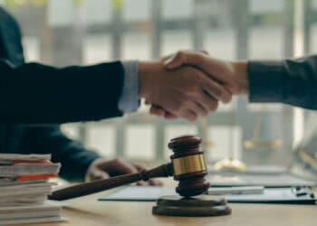 Two people shaking hands in front of Musk's X.