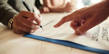 Two people signing a contract at a table, ensuring international law compliance and transparency.