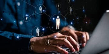 Person's hands typing on laptop, network of connected people icons displayed. Okta security breach impact. - Supply Chain News