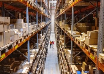 Two people walking through a warehouse full of boxes, observing the impact of China Tariffs on U.S. imports from Taiwan.