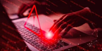 Hands typing on laptop, red warning triangle overlay. Medibank cyber attack. - Supply Chain News