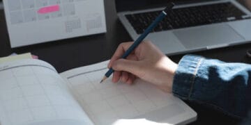 A person using a pen to write on a calendar for event-planning purposes.