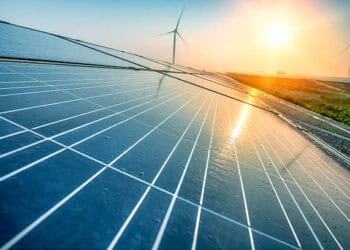 Nexamp CEO showcases solar panels with wind turbines in the background.