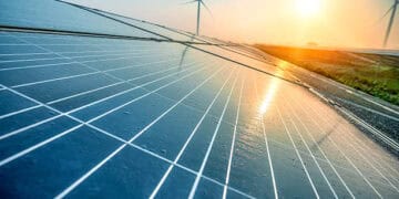 Nexamp CEO showcases solar panels with wind turbines in the background.