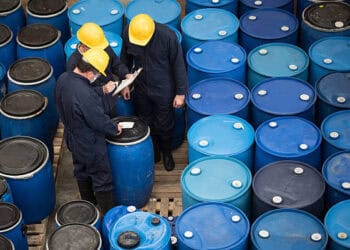 A group of workers standing next to blue barrels used for the storage of hazardous chemicals.