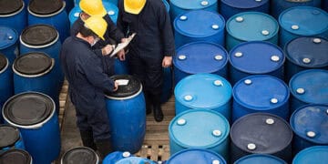 A group of workers standing next to blue barrels used for the storage of hazardous chemicals.