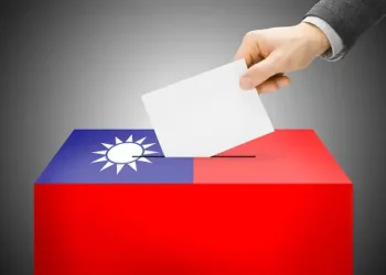 A Taiwanese man diligently inserts a paper ballot into a voting box in the midst of the presidential election, showcasing civic engagement despite prevailing trade uncertainty.