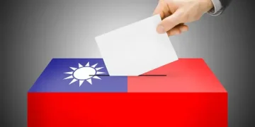A Taiwanese man diligently inserts a paper ballot into a voting box in the midst of the presidential election, showcasing civic engagement despite prevailing trade uncertainty.