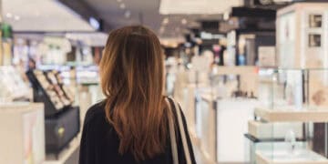 A woman browsing cosmetics in a store, considering the changing consumer dynamics and pricing strategy in the luxury market.