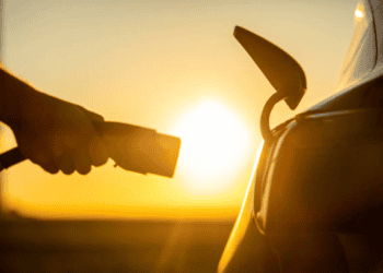 A person is charging a Chinese E.V. car at sunset, amidst increasing tariffs under the Biden administration.