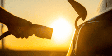 A person is charging a Chinese E.V. car at sunset, amidst increasing tariffs under the Biden administration.