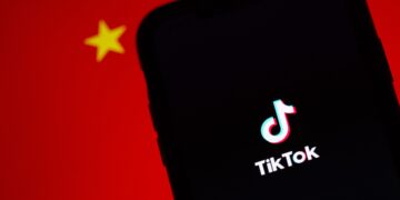 TikTok logo on smartphone screen against blurred Chinese flag background. App's endurance amidst bans. - Supply Chain News