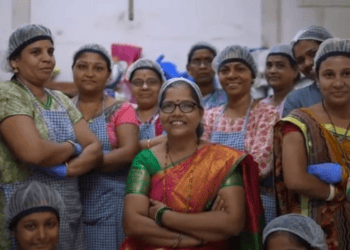 A group of women, including PatilKaki and members of Cap70 Angels, posing for a photo in a factory.