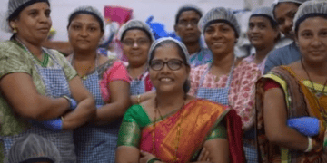 A group of women, including PatilKaki and members of Cap70 Angels, posing for a photo in a factory.