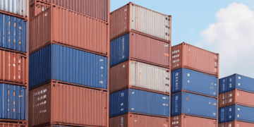 Shipping containers stacked high at a logistics facility. Trucks transport goods, boosting the supply chain workforce. - Supply Chain News