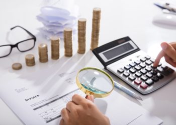 Close-up of invoice, calculator, coins, and magnifying glass; preparing for Chief Procurement Officer Summit. - Supply Chain News