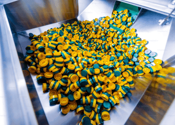 Close-up of many yellow and green plastic bottle caps in a metal chute. - Supply Chain News
