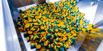Close-up of many yellow and green plastic bottle caps in a metal chute. - Supply Chain News