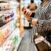Woman examining a jar of pasta sauce in a grocery store aisle, impacted by ending tariff exemptions. - Supply Chain News